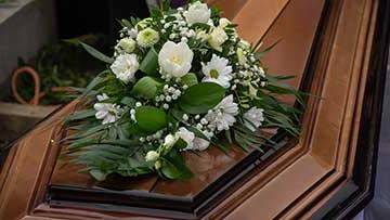 A brown wooden casket with white roses and greenery on top